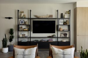 chairs and cushions in front of shelving display and tv in common space of hotel