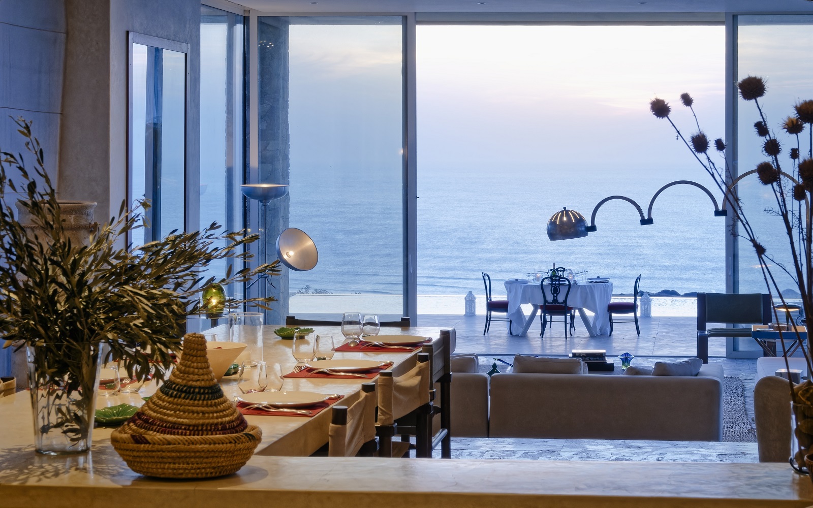 view out of villa with profile of mid century italien lamp in front of pool and dining table looking across to the sea view at La Fiermontina Ocean Morocco