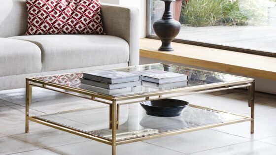 glass topped coffee table with books on it in front of cream couch with a rust patterned cushion