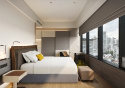 COMO Metropolitan Singapore hotel guestroom in grey and white with a yellow pillow on the bed and views across Singapore