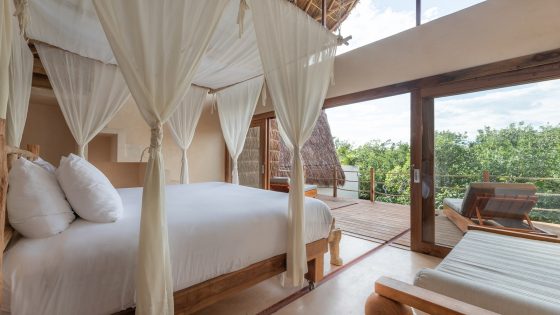 bed draped in fabric with white linen looking out over the Tulum jungle treetops at La Valise