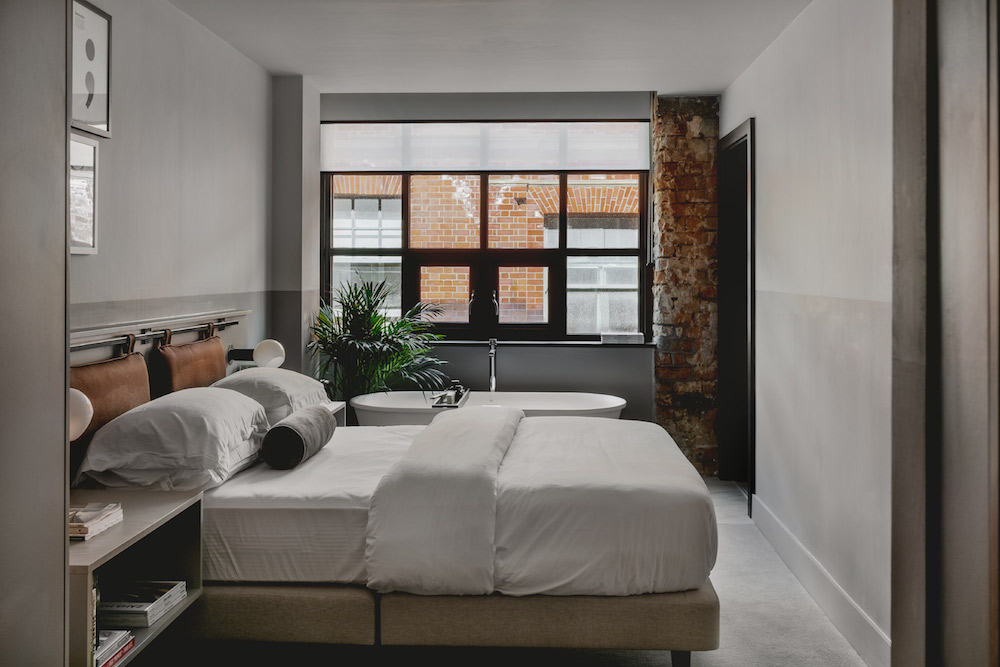 Suite with white bed, exposed brick and bath, inside LEVEN Manchester