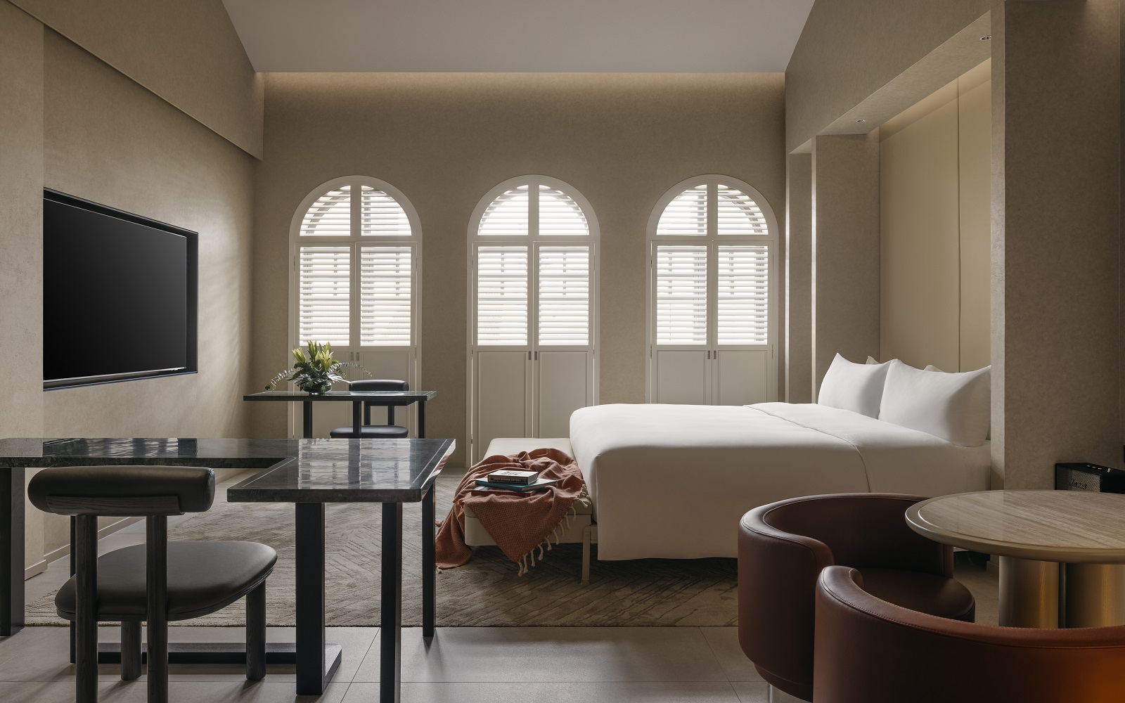 three arched shuttered windows in cream and white guestroom with wooden chair and table detail