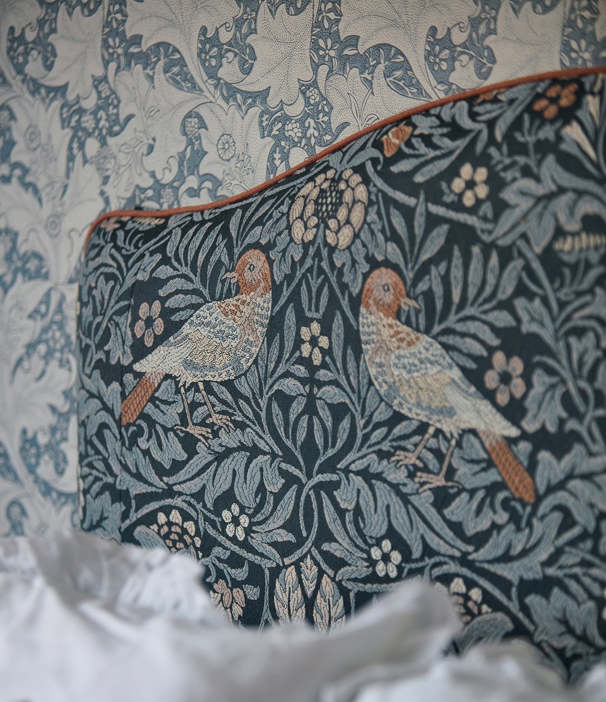 close up of a corner of an upholstered headboard in morris & Co pattern with leaves and birds in blue